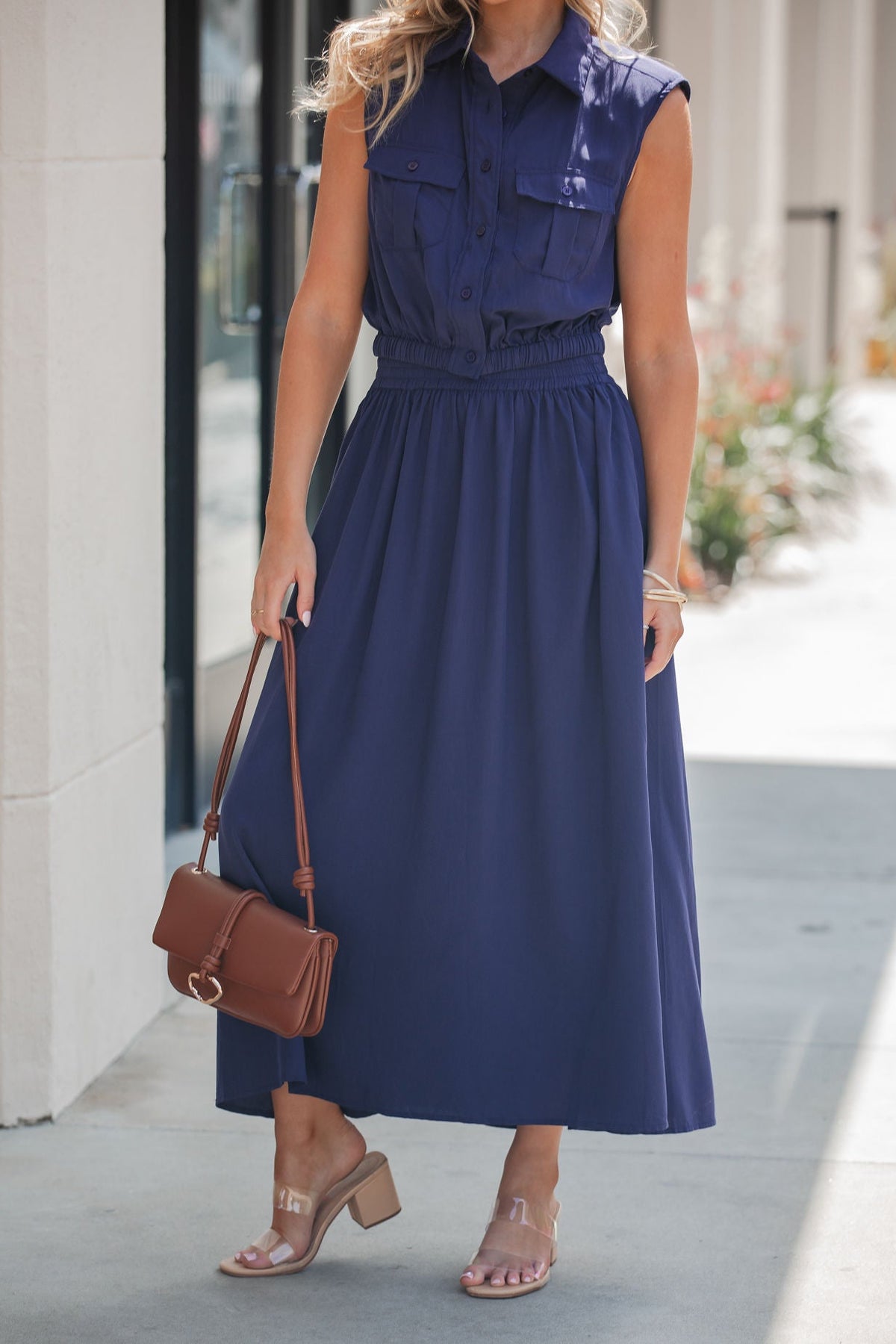 Woman in the Elan Navy Collared Button Down Top, styled with clear heeled sandals and a brown shoulder bag outdoors.