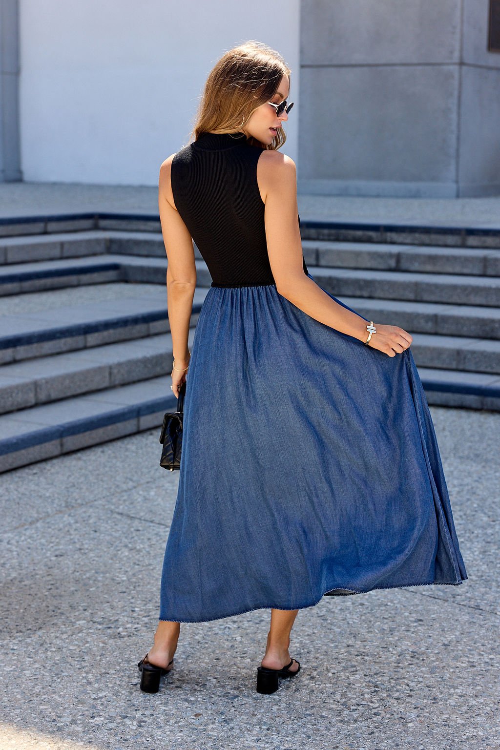 Woman in sunglasses wears the Elan Two Tone Midi Dress in navy, standing outdoors on steps and holding her skirt.