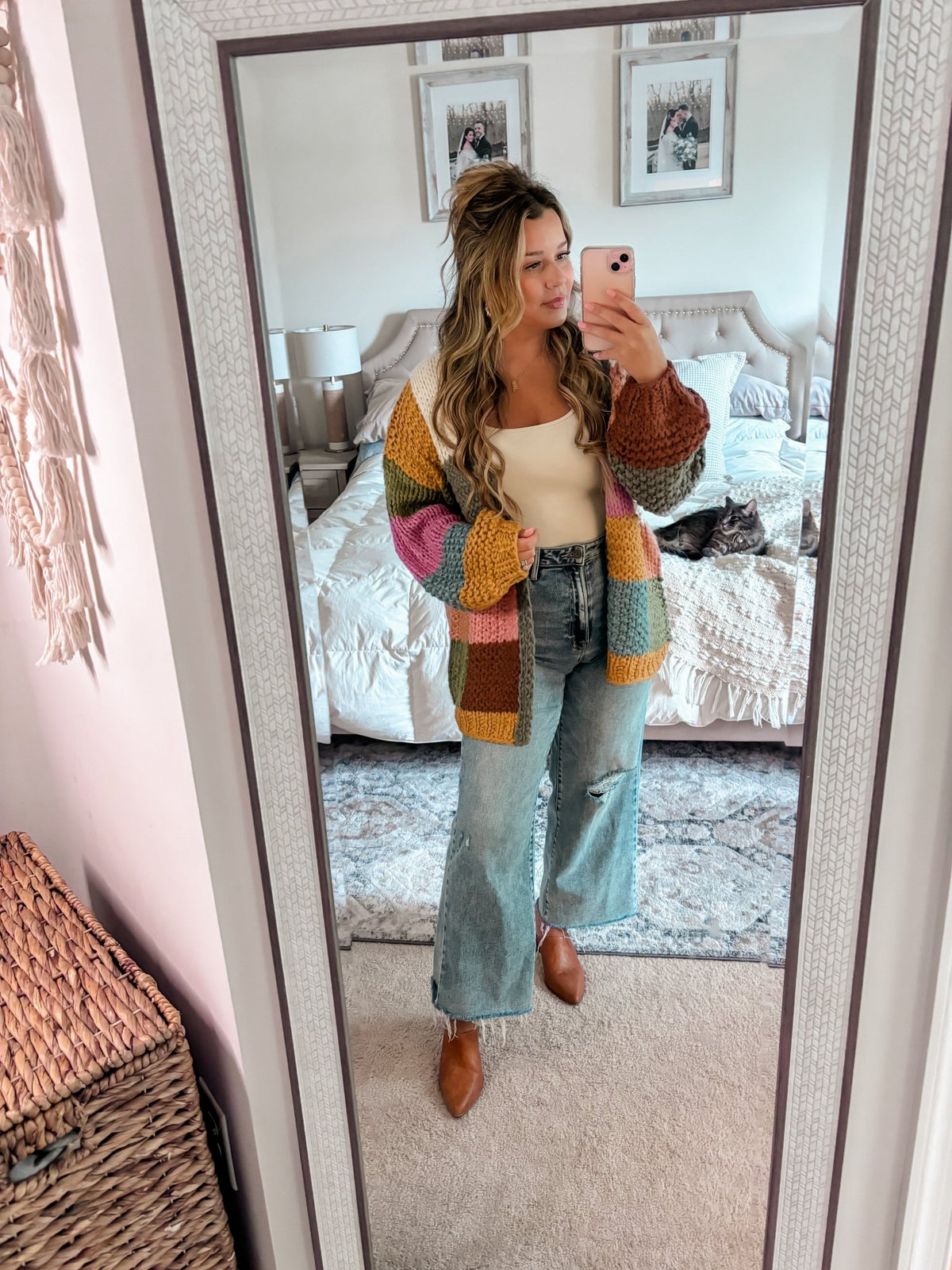 Woman taking a mirror selfie in a bedroom, wearing the Falling Leaves Olive Color Block Cardigan - FINAL SALE; cat on bed behind her.