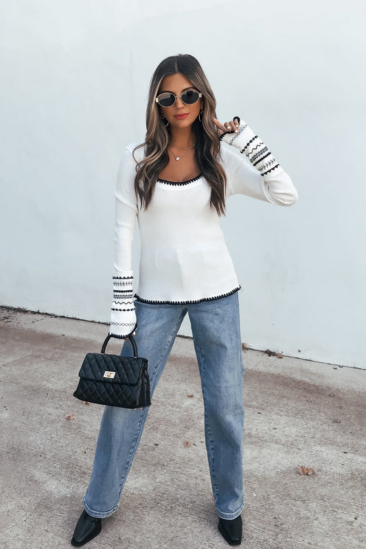 Woman in sunglasses wears a white Free People Aspen Thermal Top (pre-order), blue jeans, black heels, and holds a black quilted handbag.