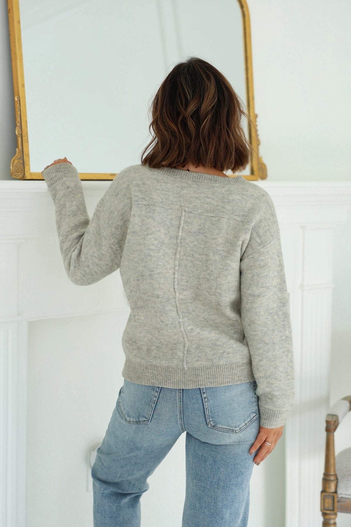 A woman in a Grey and White Heart Shape Sweater gazes thoughtfully at a picture on the wall.