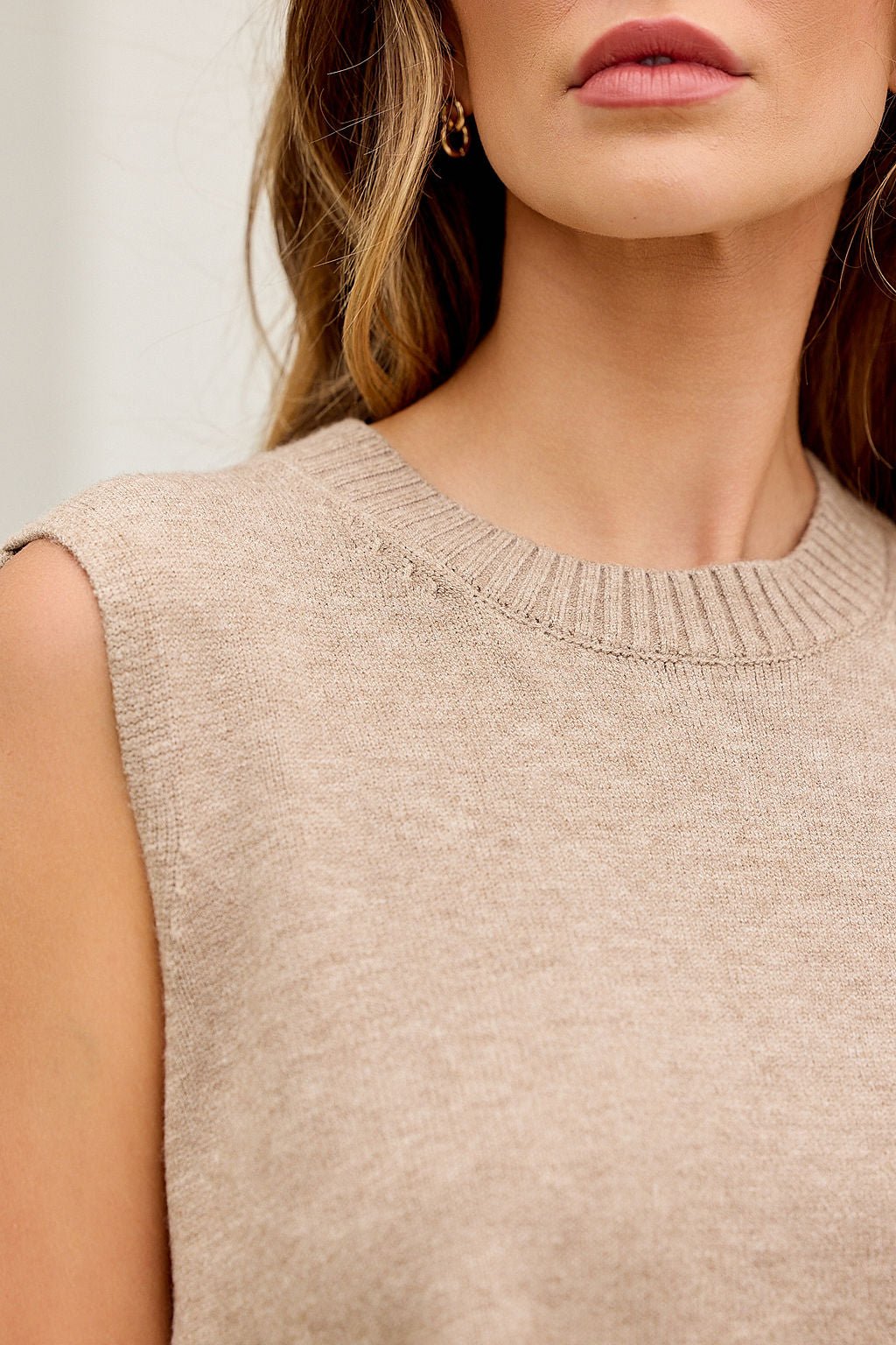 Woman in Nine To Five Cashmere Sweater, dark beige, sleeveless; loose hair, gold hoop earring; shown shoulders to lips.