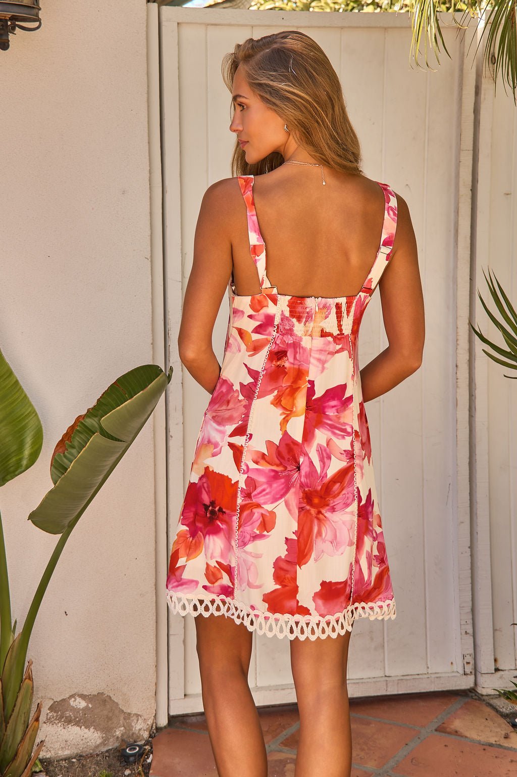 Woman in the Sweet Orchard Print Mini Dress - Pink stands outside, its botanical print and crochet lace trim blend with the garden.