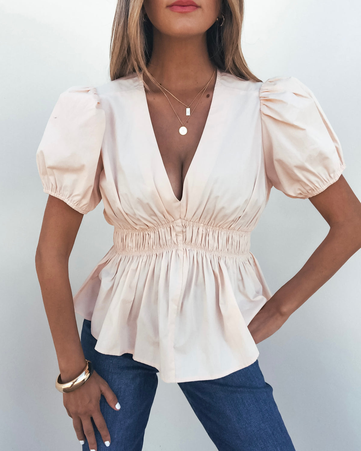 Woman wears the Blush Puff Sleeve Peplum Top - FINAL SALE with blue jeans, standing against a plain white background.