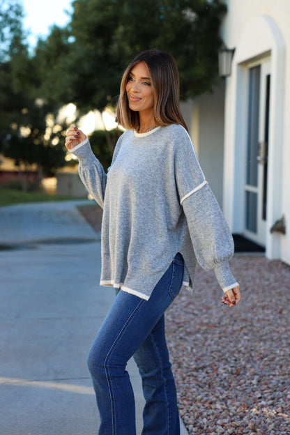 Woman smiles outside in a Grey Contrast Detail Pullover Sweater and jeans, capturing classic fall style by a white building and trees.