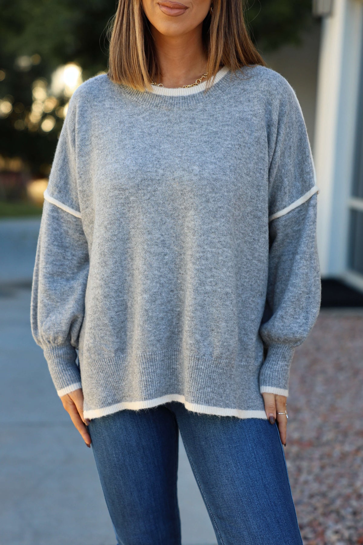 Woman wears the Grey Contrast Detail Pullover Sweater with blue jeans outdoors—an ideal pick for any fall wardrobe. Face partly out of frame.