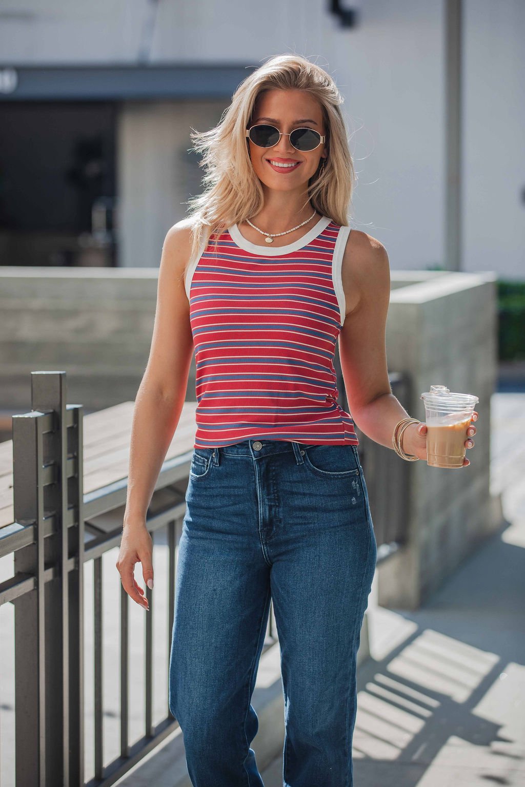 Woman in sunglasses and All-Day Stripe Tank Top - Red smiles with iced coffee outside on a sunny day.
