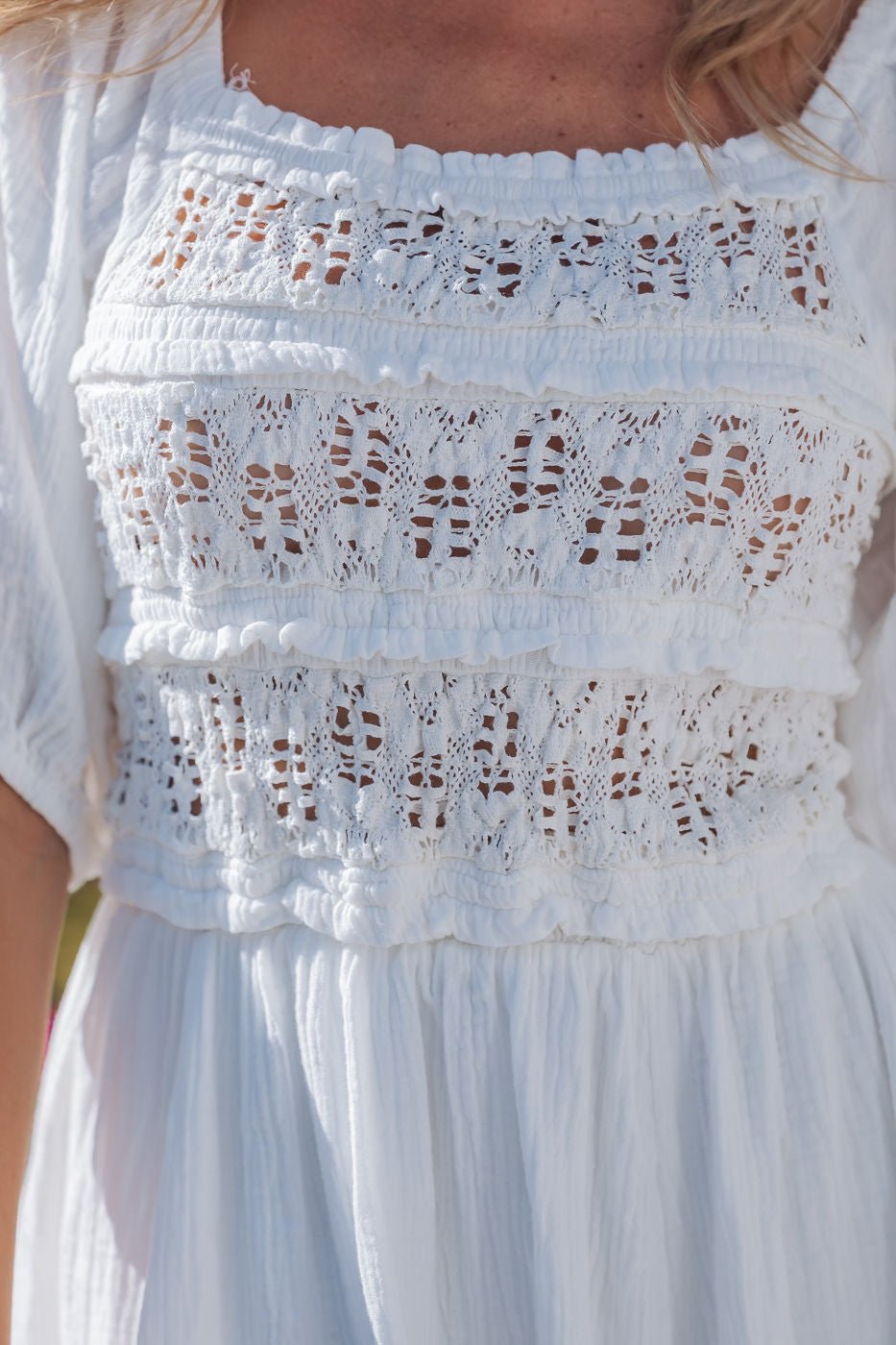 Close-up of a woman wearing the Angelica White Ruched Midi Dress - FINAL SALE with lace and crochet details on the bodice.