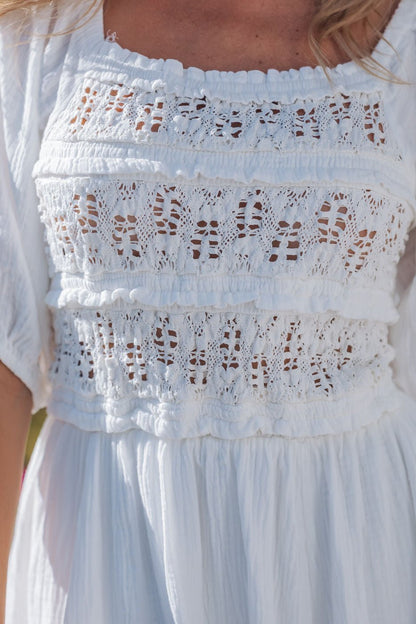 Close-up of a woman wearing the Angelica White Ruched Midi Dress - FINAL SALE with lace and crochet details on the bodice.