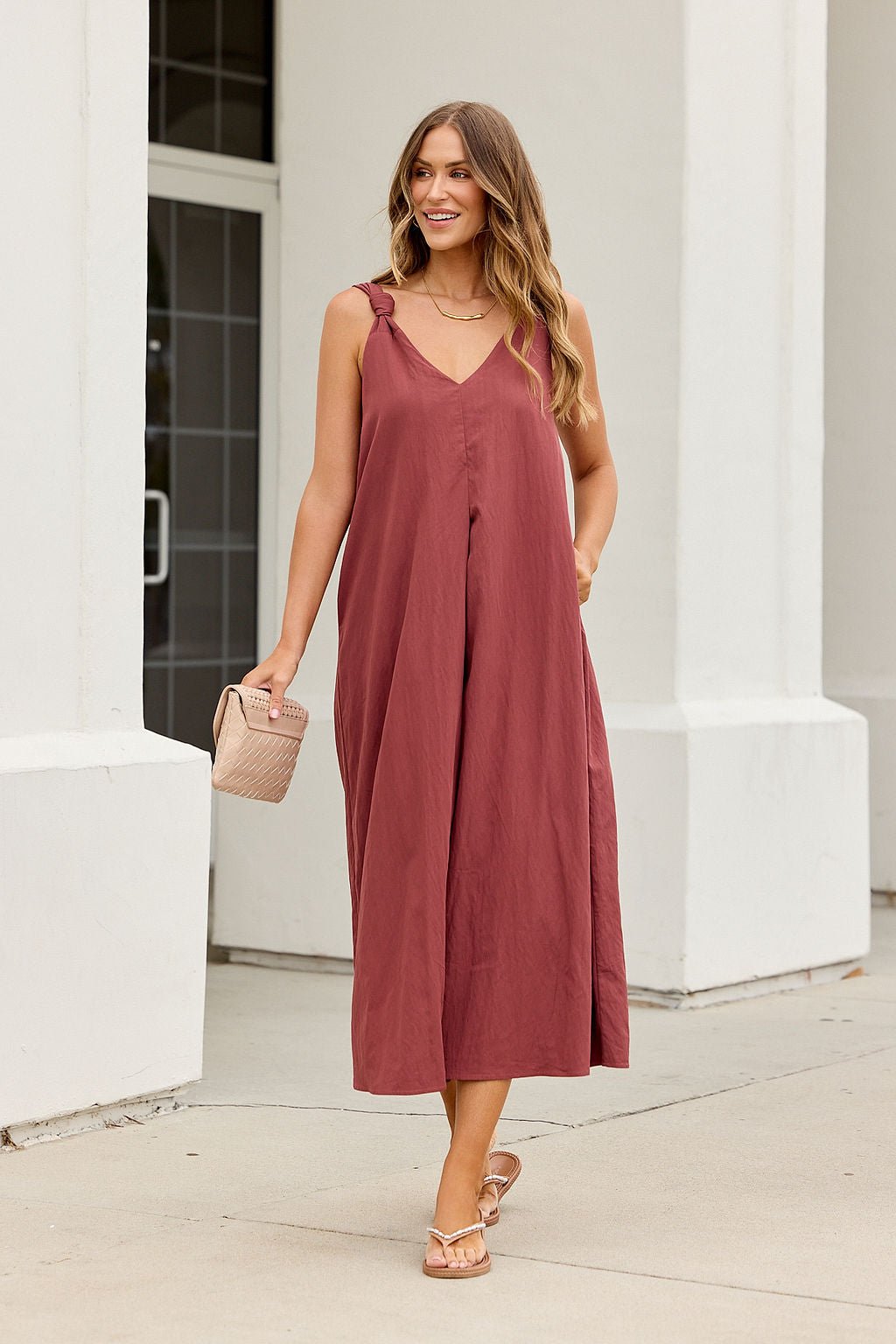Woman in the Audrey Knot Strap Midi Dress in burgundy smiles while walking outdoors near a white building.