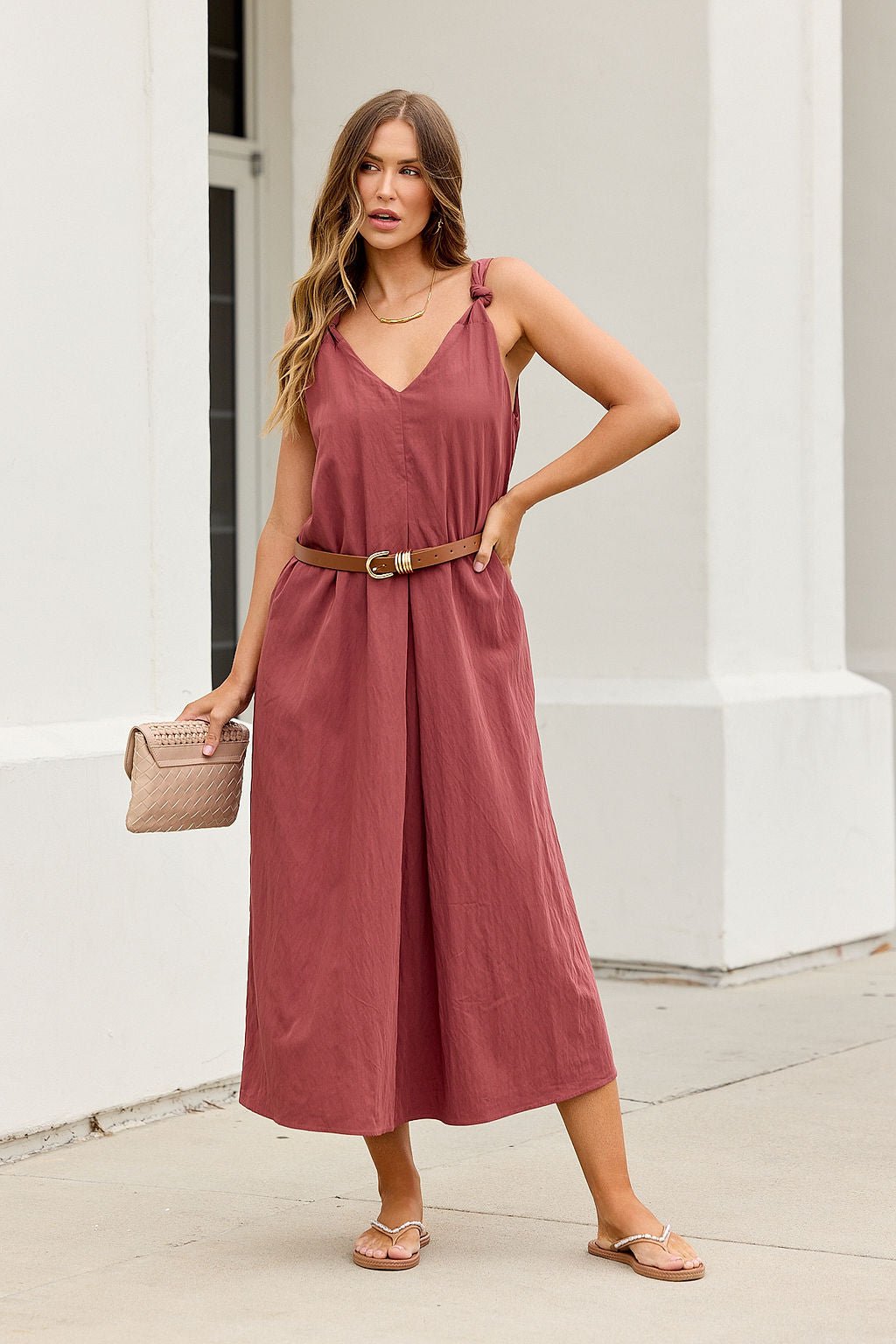 Woman wears the Audrey Knot Strap Midi Dress in burgundy, holding a purse and wearing sandals outdoors.