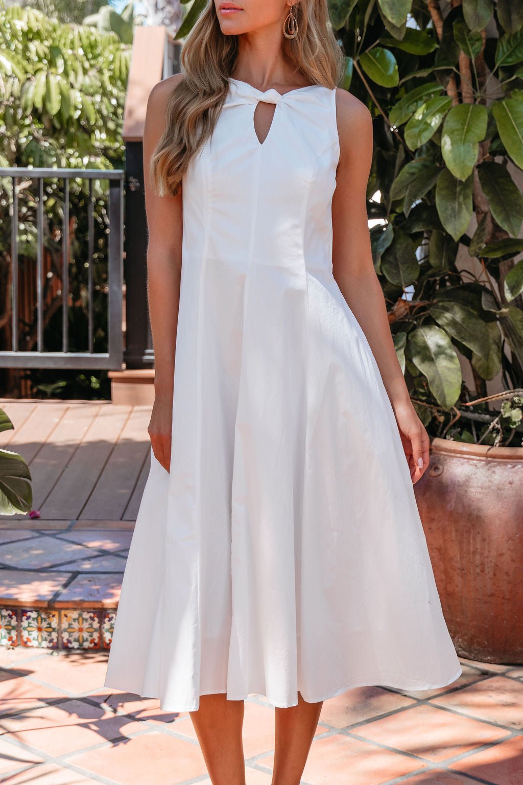 Woman in the Aureum Keyhole Midi Dress - White, perfect for special occasions, standing by potted plants and tiled steps.