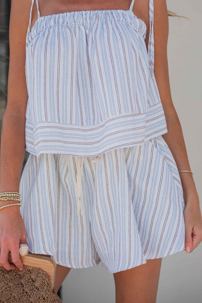 Woman wearing the Bayview Stripe Tie‑Strap Top in Blue, featuring adjustable straps; paired with matching shorts and a clutch bag.