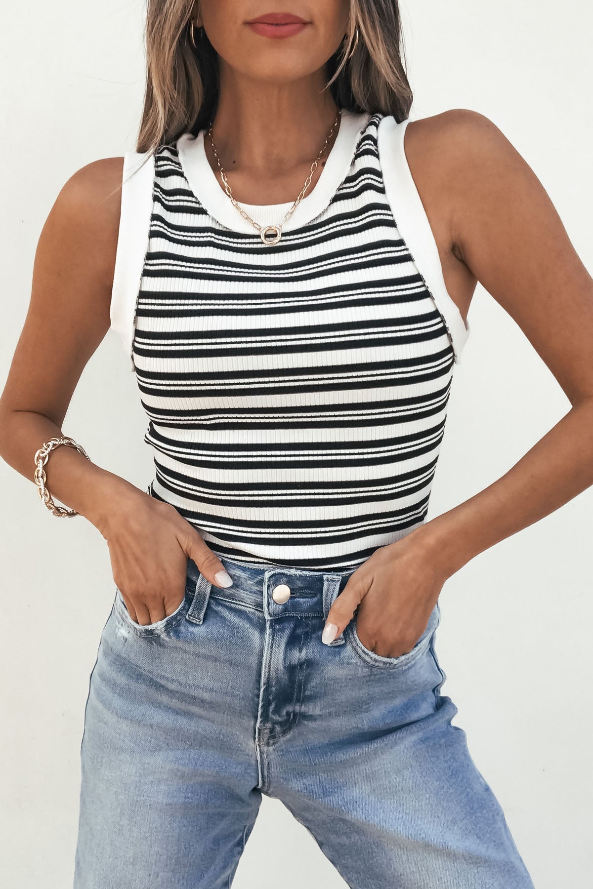 Model wears the Black and White Striped Tank Top-FINAL SALE with blue jeans, standing hands-in-pocket against a white background.