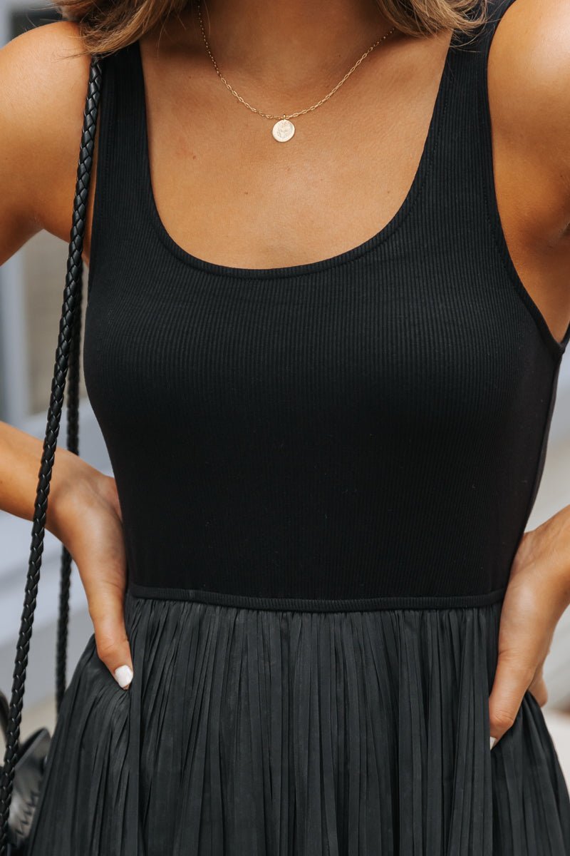 Woman in Black Scoop Neck Pleated Tank Midi Dress, hands at waist, styled with a gold necklace.