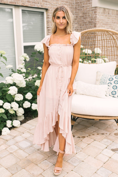 Woman in Blush Off the Shoulder Button Down High Low Maxi stands on patio near hydrangeas and a wicker chair with white cushions.