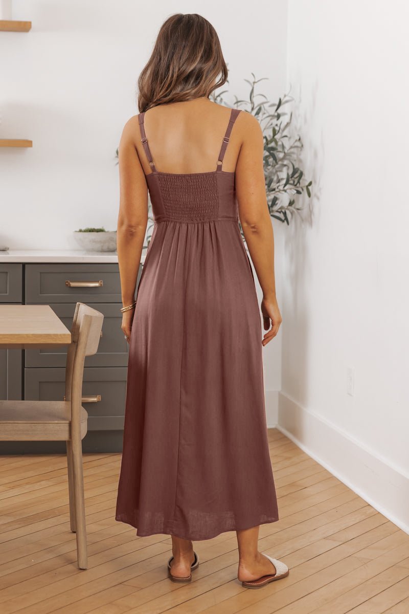 Woman wears the Deep Mauve V Neck Linen Midi Dress-FINAL SALE, standing in a modern, light-toned kitchen with her back to the camera.