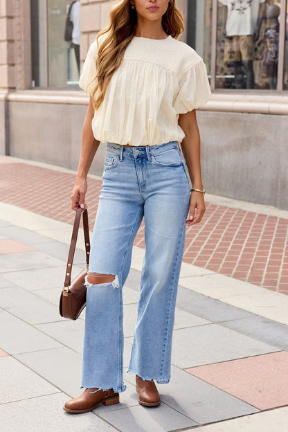 Woman in an ivory Bubble Hem Short Sleeve Top, ripped light blue jeans, brown shoes, and a brown bag walking on a city sidewalk.