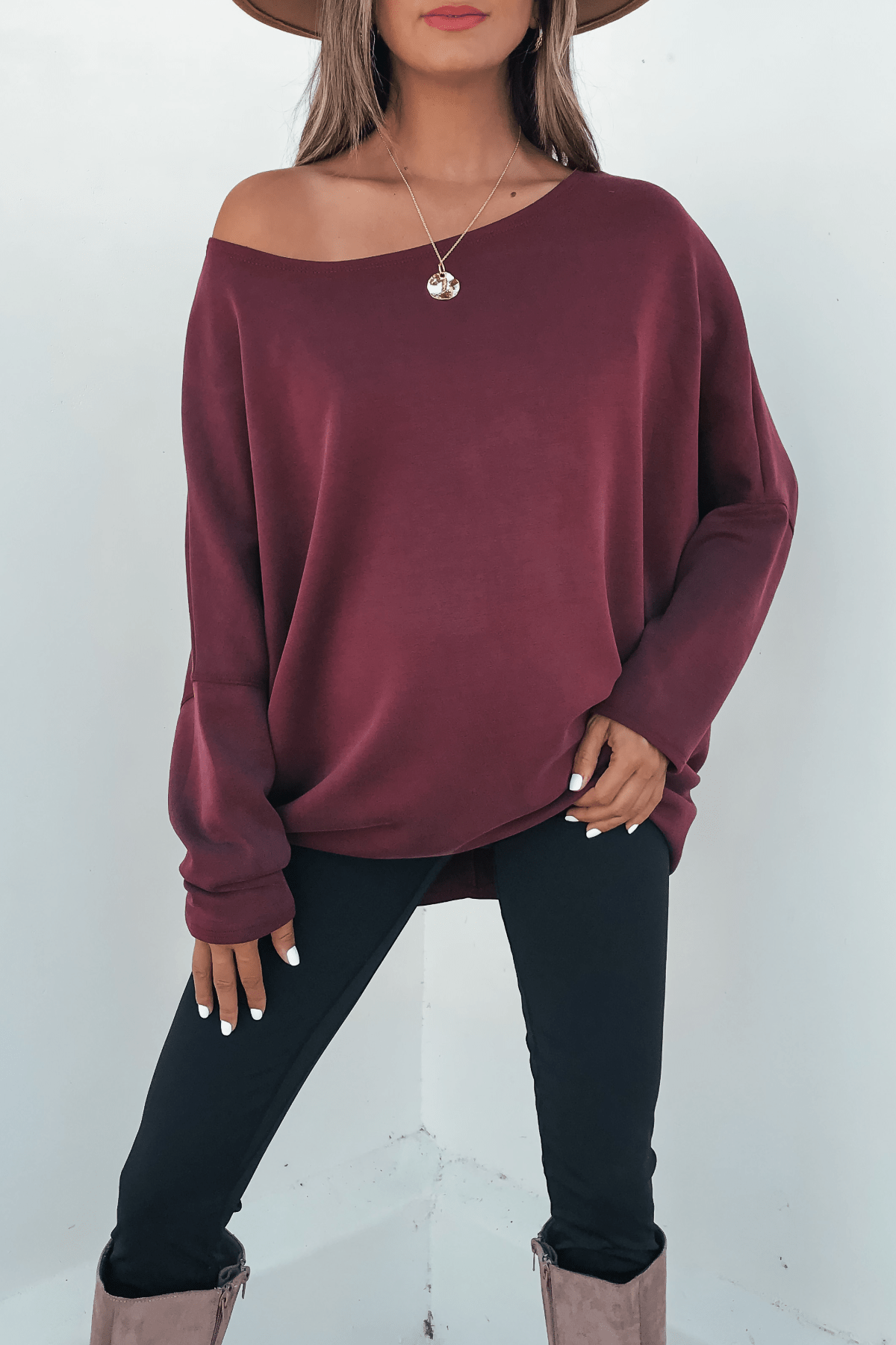 Woman in a Burgundy Soft Cloud Scuba Pullover, black pants, taupe boots, and hat stands against a white background. Made in USA.