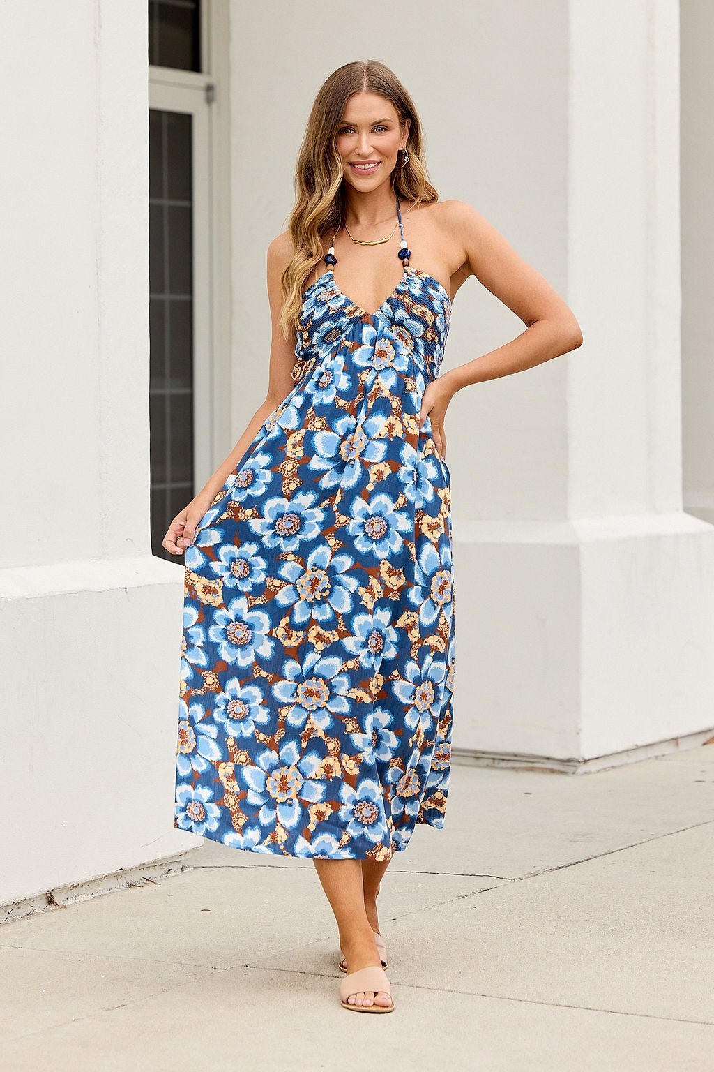 Woman in the Catalina Halter Midi Dress - Navy stands outside, smiling with one hand on her hip, wearing sandals.