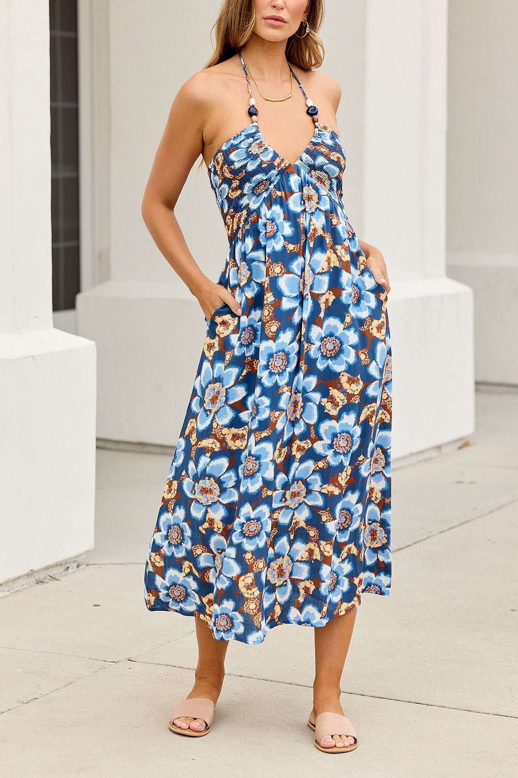 Woman in the Catalina Halter Midi Dress - Navy, tan sandals, stands by a white building on the sidewalk.
