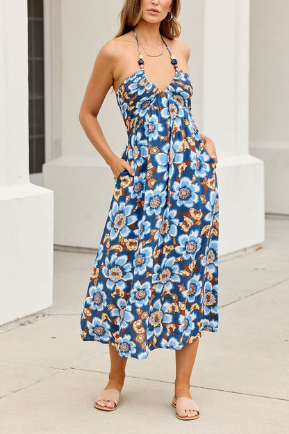 Woman in the Catalina Halter Midi Dress - Navy, tan sandals, stands by a white building on the sidewalk.