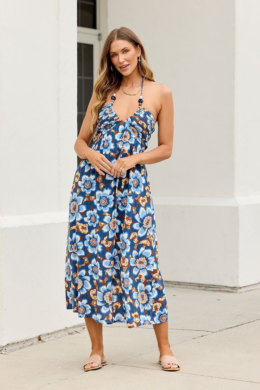 Woman wears the Catalina Halter Midi Dress in navy, smiling outside near a white building.