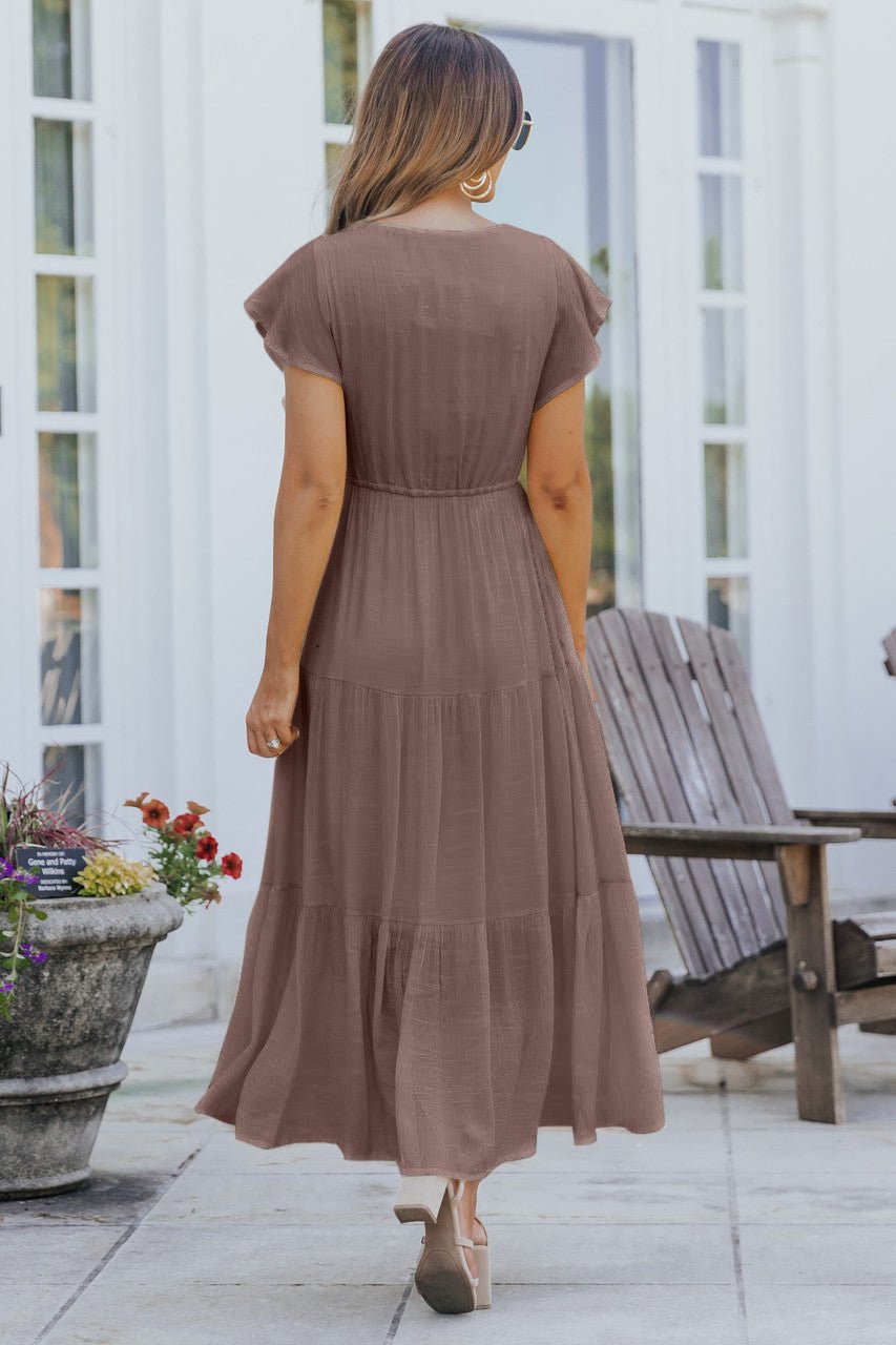 Woman in a Celine Crochet Lace Tiered Boho Midi Dress stands outdoors on a patio, facing away, near wooden chairs and a potted plant.