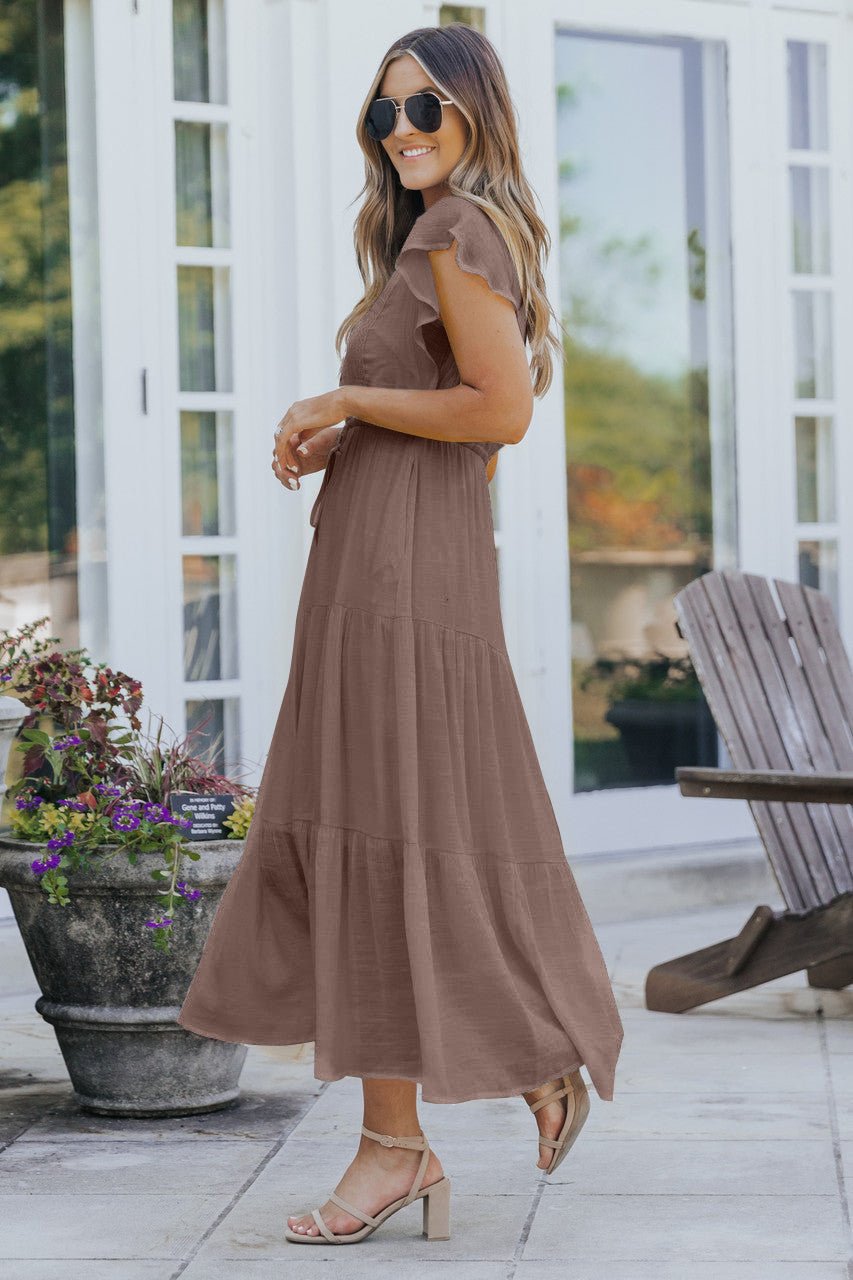 Woman in a Celine Crochet Lace Tiered Boho Midi Dress stands on a patio, smiling with sandals and sunglasses near flowers and wooden chairs.