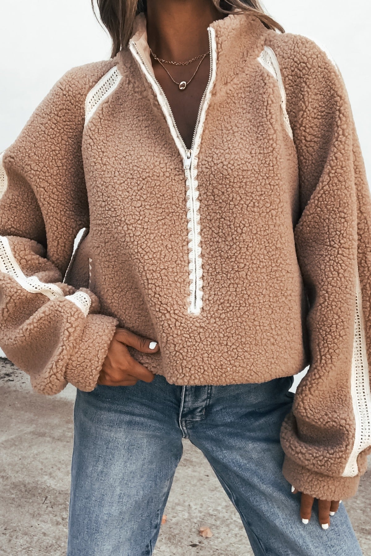 Woman wears the Contrast Quarter Zip Jacket - Sand with white trim and blue jeans, posing with one hand on her hip.