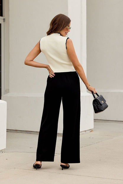 Woman outdoors, facing away, in black pants and Cream Contrast Sweater Tank Top, holding a small purse and wearing sunglasses.