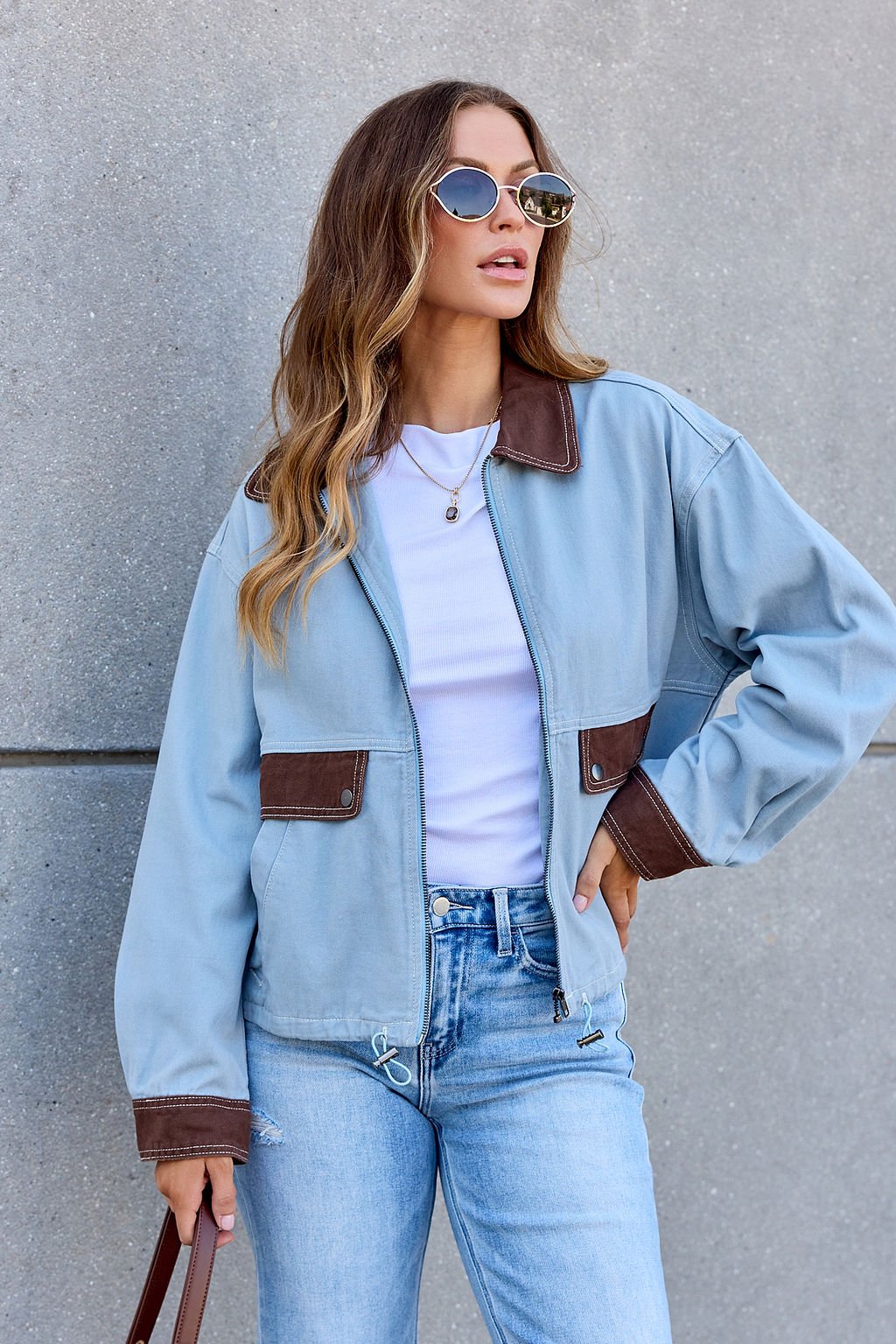 Woman in sunglasses, white shirt, jeans, brown bag, and the Contrast Trim Jacket - Dusty Blue with brown accents.