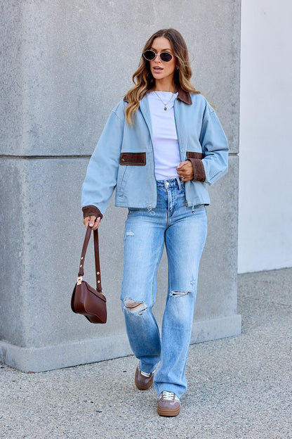 Woman in sunglasses wears a Contrast Trim Jacket - Dusty Blue, white shirt, ripped jeans, sneakers, and holds a brown purse outdoors.