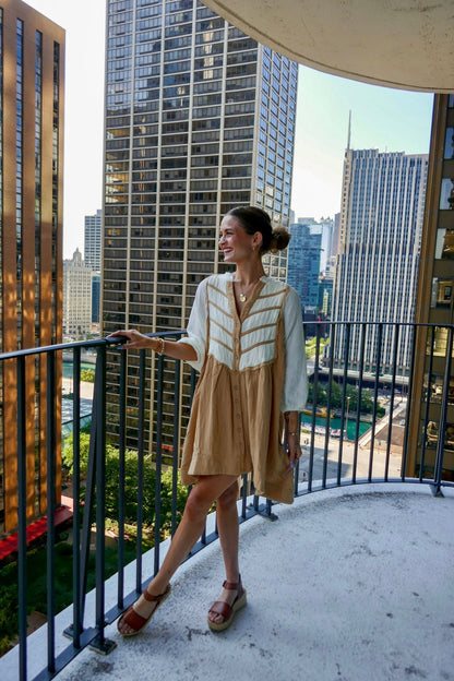 Woman in a Cream Color Block Tunic Dress-FINAL SALE smiles on a high balcony with tall city buildings behind her.