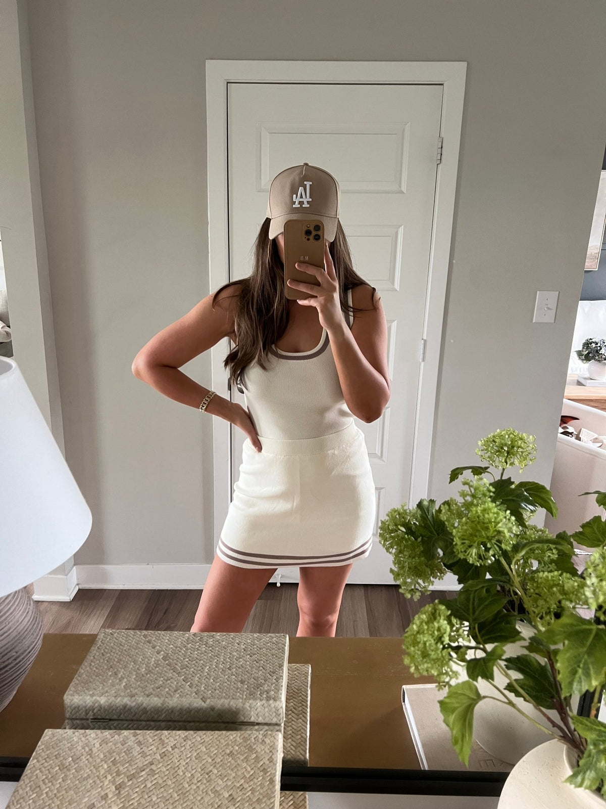 Woman in Cream Contrast Trim Tank Top-FINAL SALE and beige LA cap takes mirror selfie in modern room with green plant and decor.