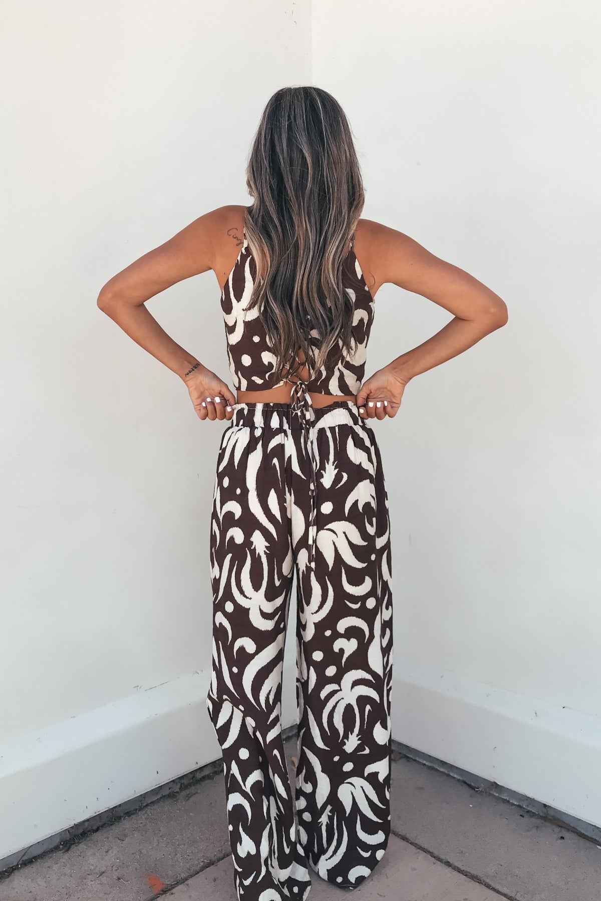 A woman with long wavy hair models the Eda Print Cami Tank and Pants Set in brown with adjustable straps and wide-leg pants.