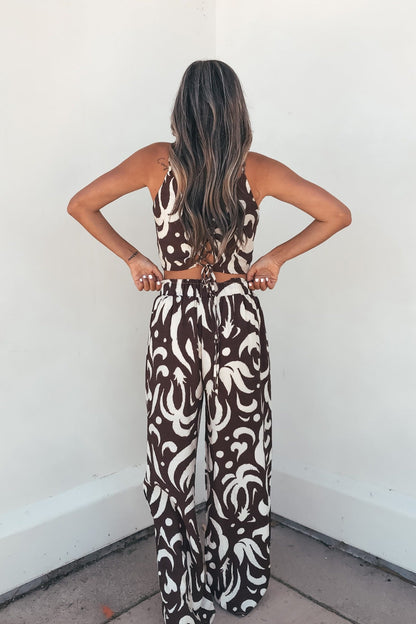 A woman with long wavy hair models the Eda Print Cami Tank and Pants Set in brown with adjustable straps and wide-leg pants.