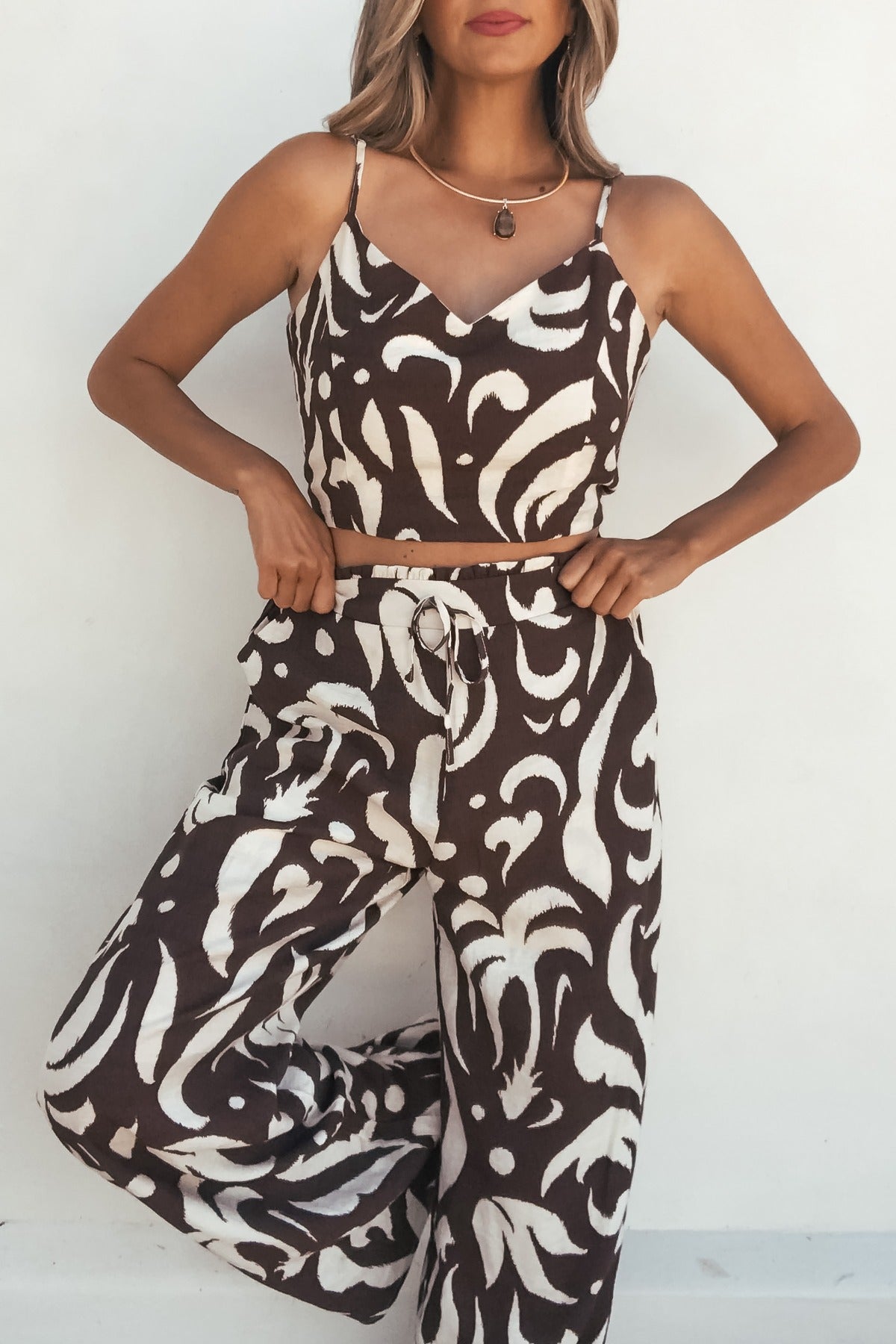 Woman wears the Eda Print Cami Tank and Pants Set in brown with adjustable straps and wide leg pants against a white background.