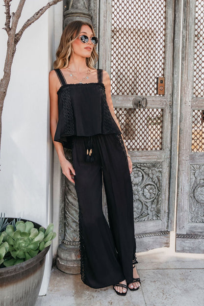 Woman in sunglasses wearing ELAN Black Lace Trim Wide Leg Pants, standing by ornate doors next to a potted plant.