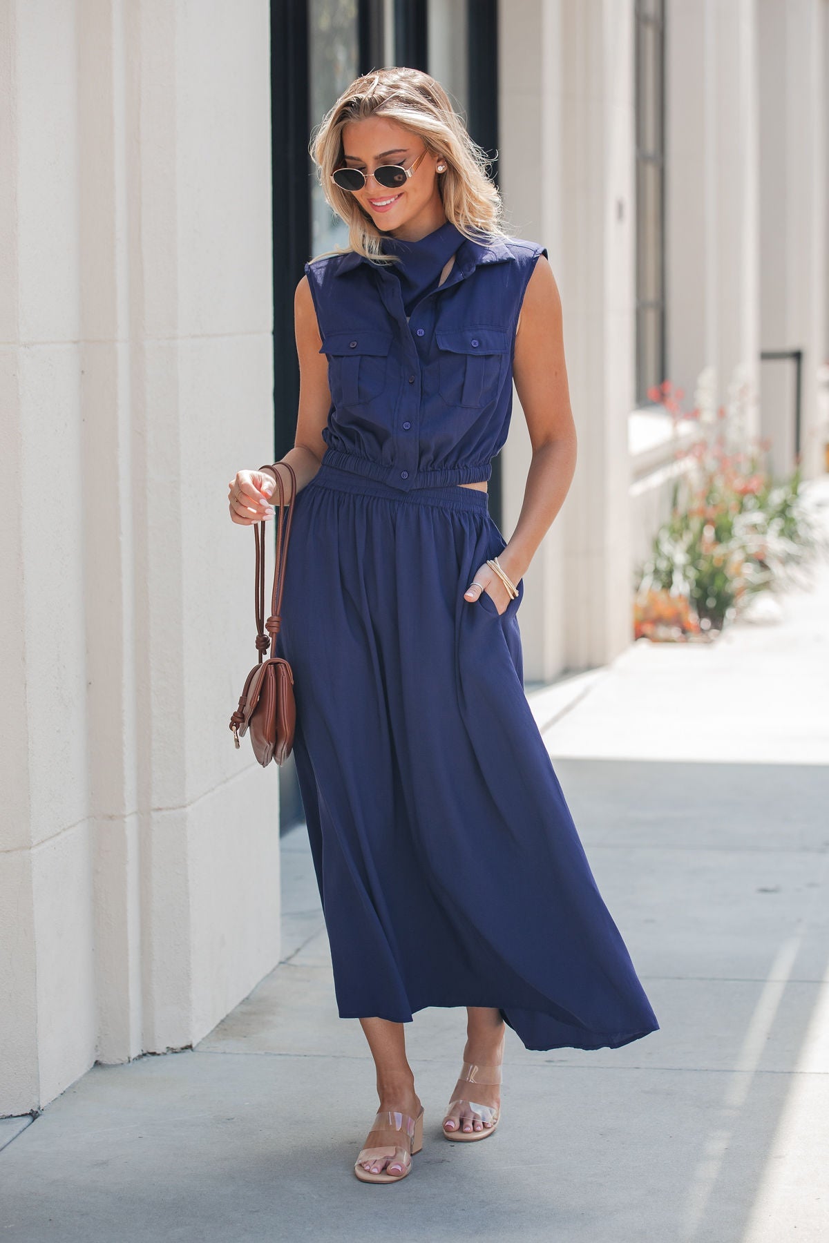 Woman in an Elan Collared Button Down Top - Navy walks on a sunny sidewalk, sunglasses and brown handbag in hand.