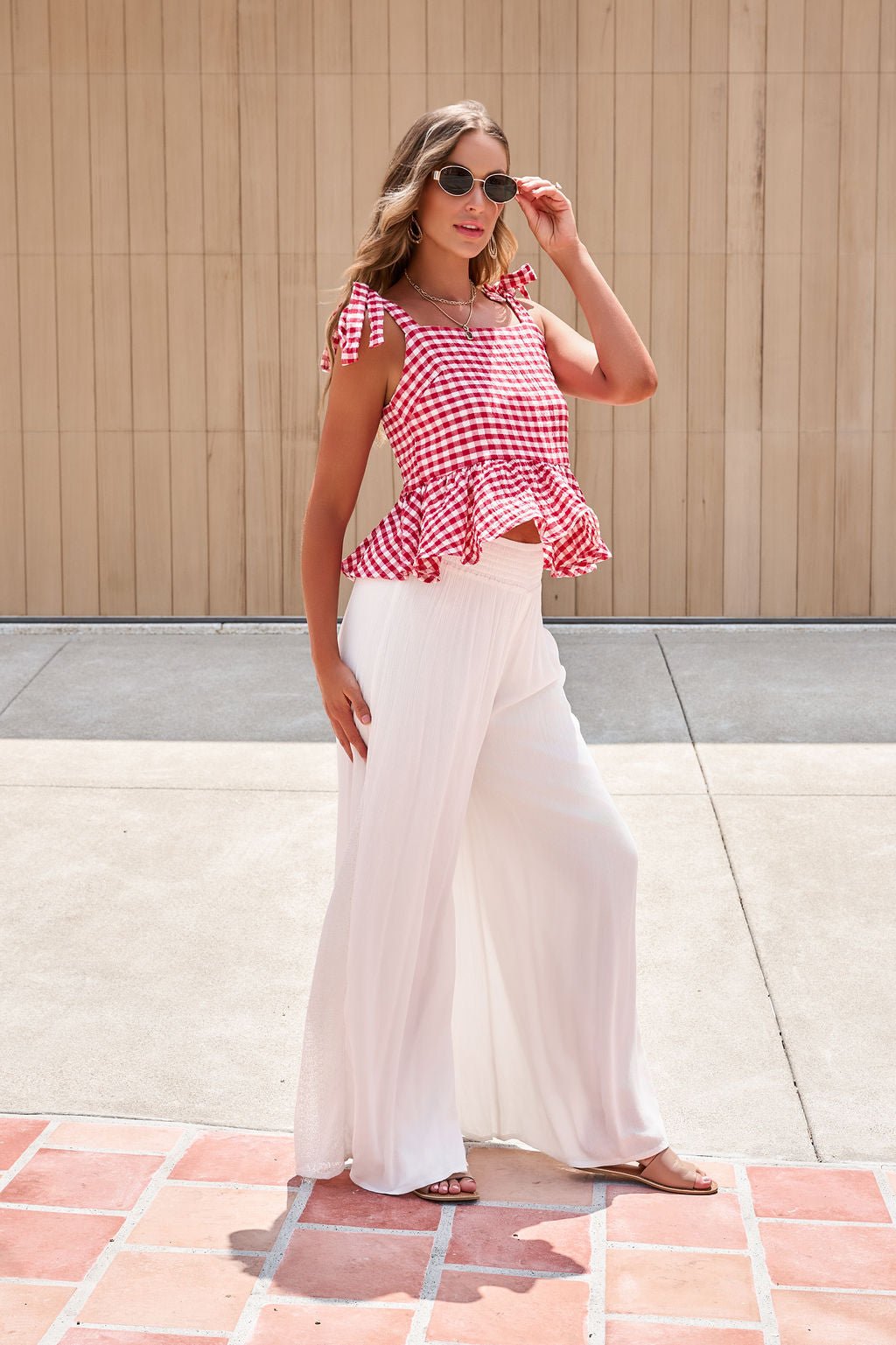 Woman in sunglasses, red gingham ruffle top, and Elan Flowy Wide Leg Pants - Ivory stands on a sunny patio.