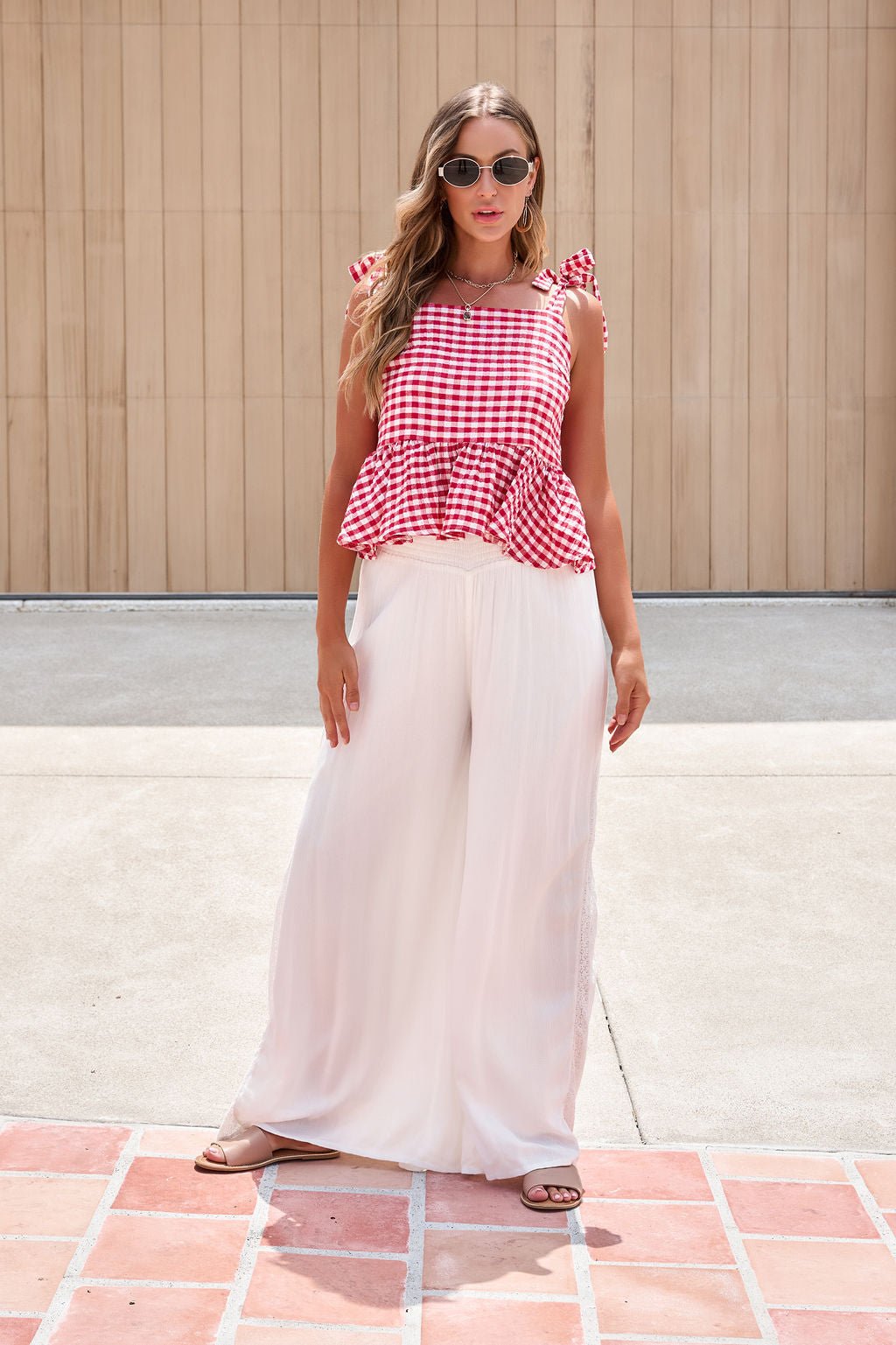 Woman in sunglasses, red gingham top, and Elan Flowy Wide Leg Pants - Ivory stands on a sunny paved area.