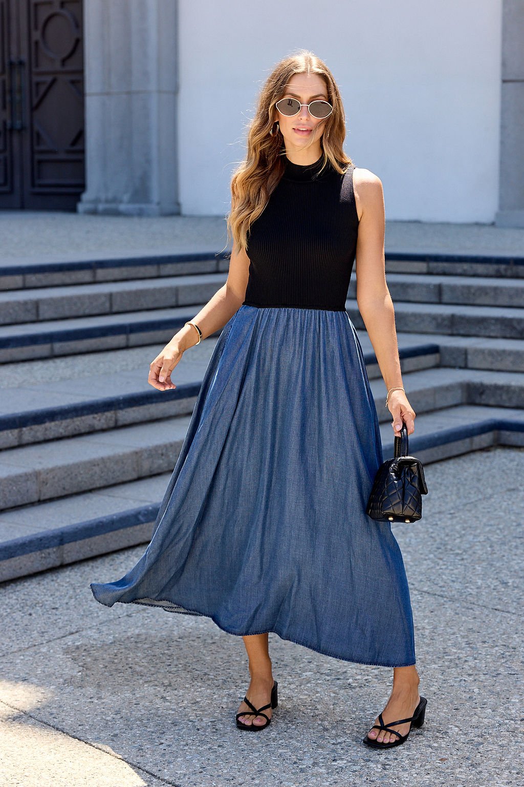 Woman in sunglasses wears Elan Two Tone Midi Dress - Navy, holding a black bag while walking outdoors.