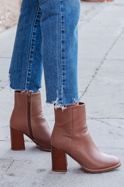Person wearing frayed hem blue jeans and Evelyn Taupe Leather Heeled Ankle Booties, standing on a sidewalk.