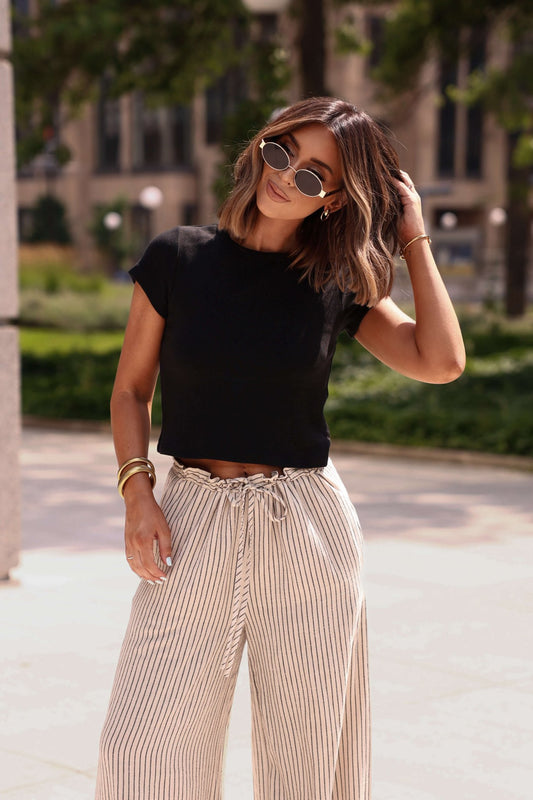 Woman wearing sunglasses and the Everyday Essential Black Tee-FINAL SALE outdoors, touching her hair amid lush greenery.