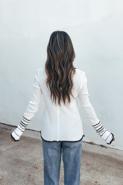 Person with long wavy hair in a white Free People Aspen Thermal Top and blue jeans, standing outdoors facing away.