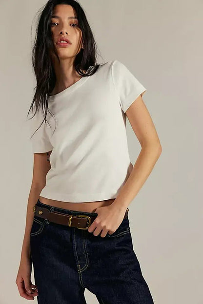 Woman with long dark hair models the Free People Atlas Crew Tee - Ivory with dark jeans, highlighting its fitted shape against a plain backdrop.