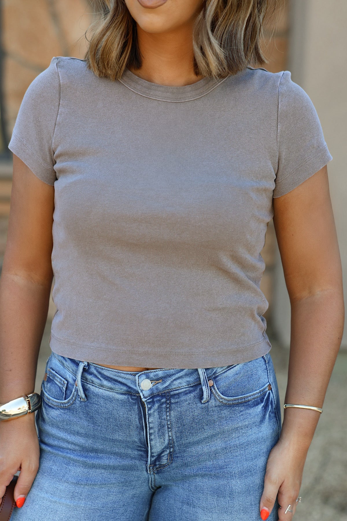 Woman in a mocha Free People Atlas Crew Tee with crew neck and blue jeans, standing outdoors with relaxed hands.