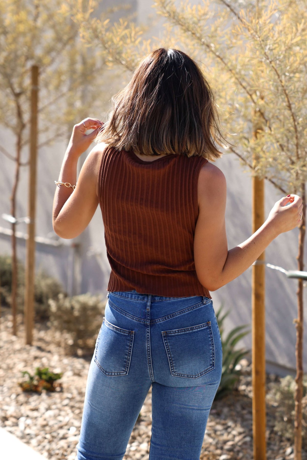 A woman wears the Free People Brown Tilly Vest Top and blue jeans outdoors, her shoulder-length hair turned away.