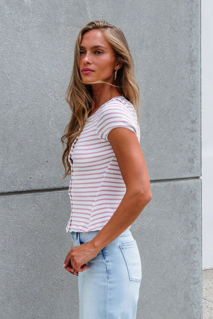 Woman with long hair in the Free People Stripe Most Wanted Top - Mauve stands by a gray concrete wall in light jeans.